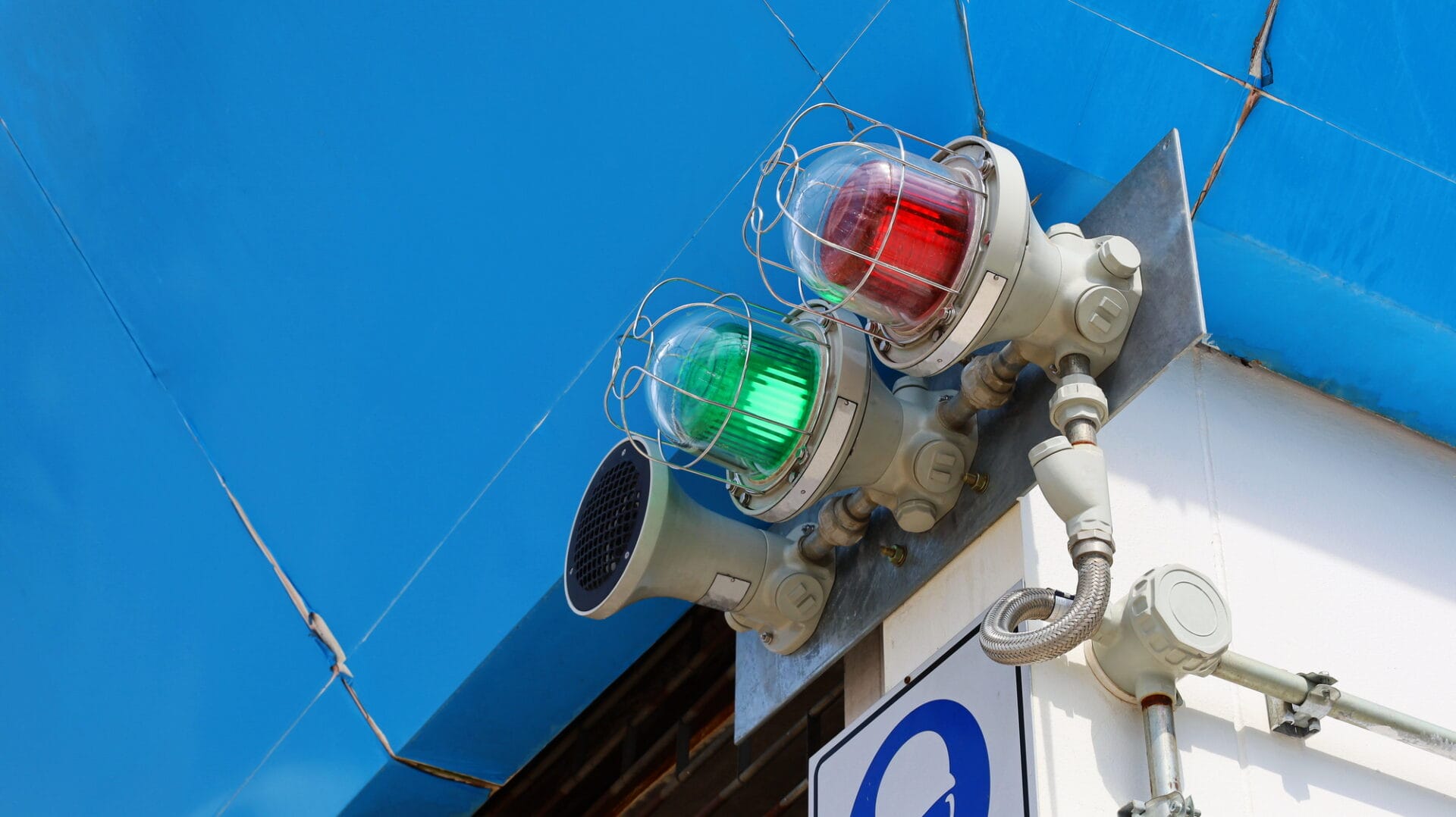 Green and red industrial signal lights mounted on a metal fixture against a blue sky.