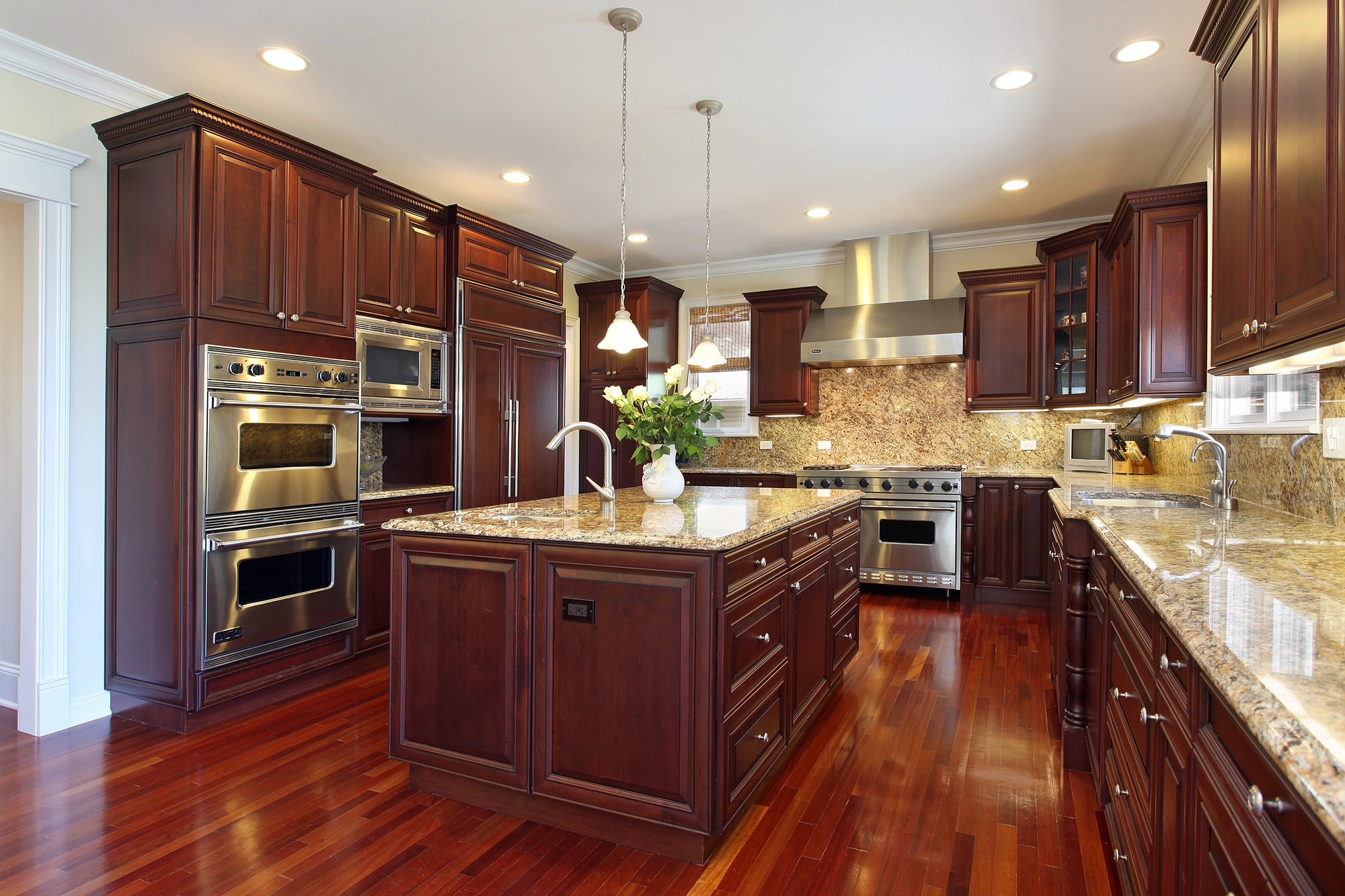 Spacious kitchen with dark wood cabinets, granite countertops, stainless steel appliances, and a central island with pendant lighting.