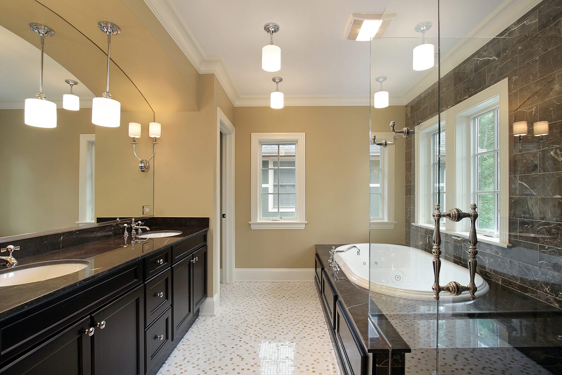 A luxurious bathroom with double sinks, large mirror, bathtub, and dark cabinetry. It has polished white tile flooring and multiple pendant lights.